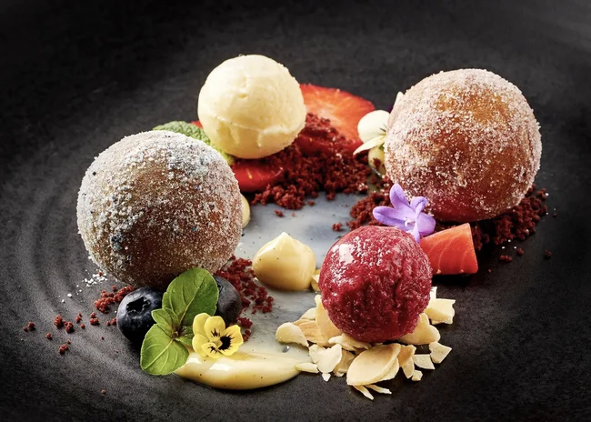 Der Salnerhof – das Hotel in Ischgl Kunstvoll angerichtetes Dessert mit Kugeln, Beeren, Blüten und Creme auf schwarzem Teller