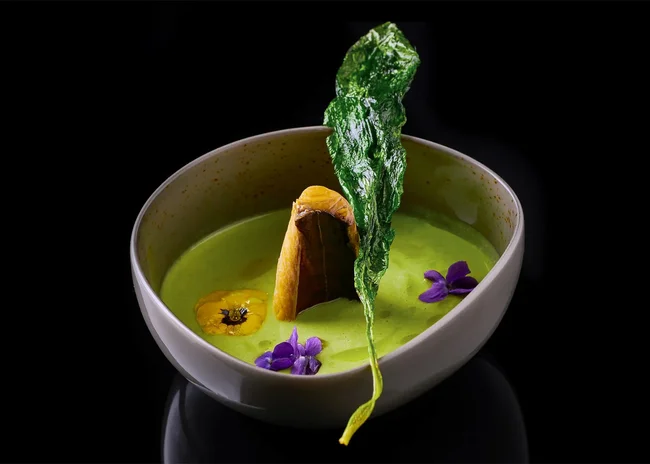 Der Salnerhof – das Hotel in Ischgl Grüne cremige Suppe mit essbaren Blüten und knusprigem Blatt in weißer Schale
