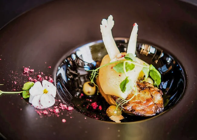 Der Salnerhof – das Hotel in Ischgl Kunstvoll angerichtetes Gourmetgericht mit essbaren Blüten und Kräutern auf schwarzem Teller